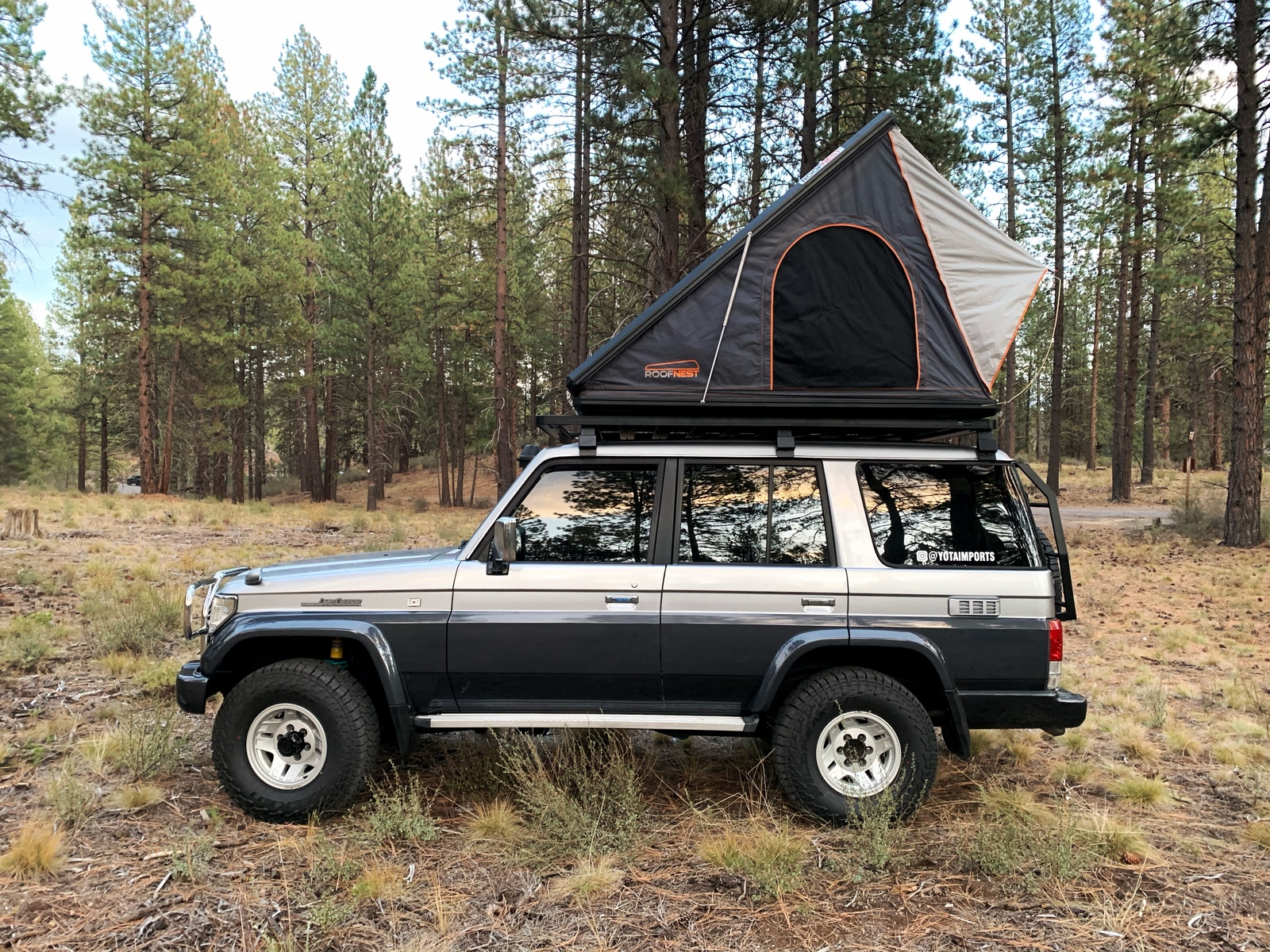 Two-tone Prado Land Cruiser with rooftop tent in the pines